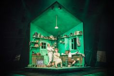 people are sitting on the stage in front of a green room with shelves and cupboards