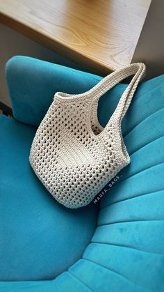 a crocheted white purse sitting on top of a blue couch next to a wooden table