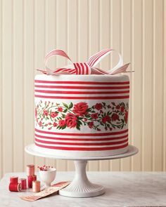 a red and white cake decorated with flowers on a table next to twine spools