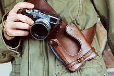 a man holding a camera in his right hand and wearing a leather belt around his waist