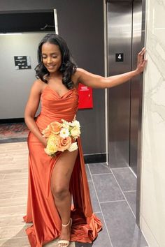 a woman in an orange dress standing next to a wall with her hand on the door