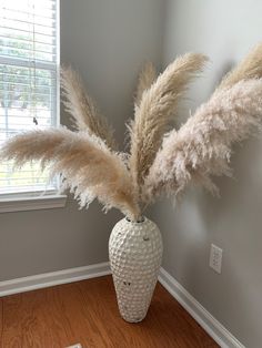 a vase with some dry grass in it on a wooden floor next to a window