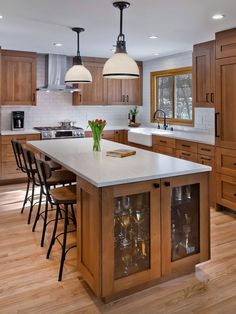 a large kitchen with wooden cabinets and white counter tops, an island with wine glasses on it