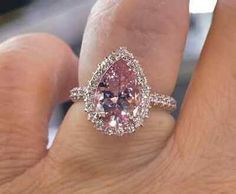 a woman's hand holding a pink diamond ring