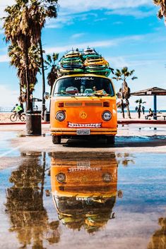 an orange van with surfboards on top parked in front of palm trees