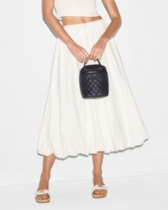 a woman wearing a white skirt and crop top holding a black purse in her hand