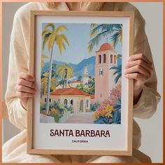 a woman holding up a framed poster with the words santa barbara in front of her