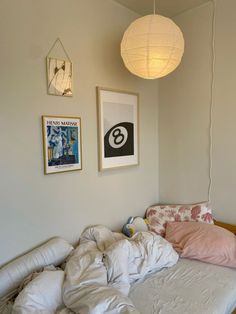 an unmade bed in a room with pictures on the wall and lamps above it