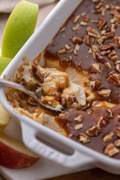 an apple and pecan dessert in a white casserole dish with a spoon