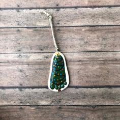 a ceramic christmas tree ornament hanging from a string on a wooden surface with other ornaments around it