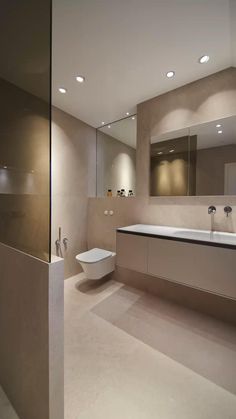 a bathroom with a toilet, sink and mirror in it's center wall is lit by recessed lights