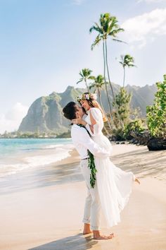 a bride and groom kissing on the beach with palm trees in the background at their wedding