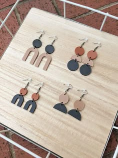 six pairs of earrings are displayed on a wooden table with metal bars in the background