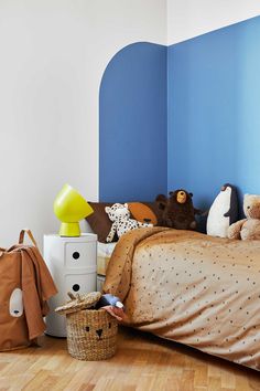 a child's bedroom with blue walls and wooden floors, stuffed animals on the bed