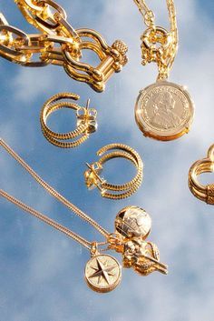 many different types of gold jewelry hanging in the air on a cloudy day with blue sky