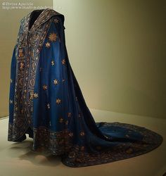 an elaborate blue and gold dress on display in a museum case with a white wall behind it