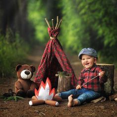 a little boy sitting on the ground next to a teddy bear and teepee tent