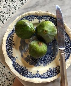 three green fruit sitting on top of a blue and white plate next to a knife