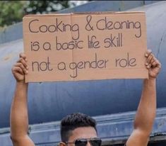 a man holding up a sign that says cooking & cleaning is a basic life skill not a gender role