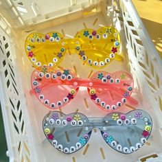 three pairs of colorful sunglasses sitting on top of a white plastic container with buttons and flowers