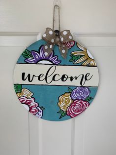 a welcome sign hanging on the front door with polka dots and flowers painted on it