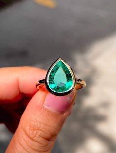 a person holding a ring with a green stone in it's middle and the top half of their finger