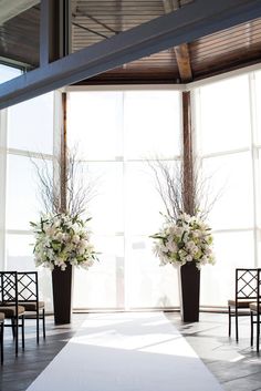 two tall vases filled with white flowers on top of a floor next to chairs