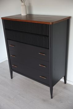 a black dresser with three drawers and two vases on it's top shelf