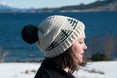 a woman standing in the snow wearing a white hat with green pom - poms