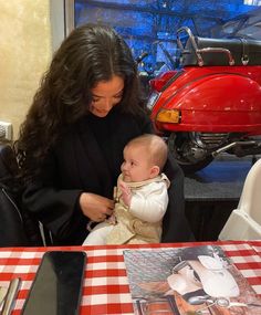 a woman sitting at a table holding a baby