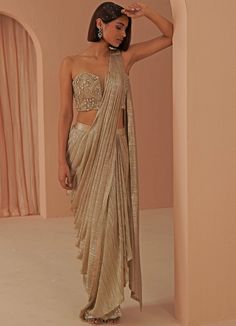 Glam Vibes in this gold gleam pleated drape saree teamed with a corset encrusted with stone work and zardosi in gold hues. This ensemble is a ready to wear saree for your ease ! Blouse can have straps added for ease. Composition: Saree - Lycra Net, Blouse- Net , Lining-Butter Crepe All products can be customised for sleeves, length of blouse and neck design Delivery : 4-6 weeks as the product is hand crafted. Check Size Guide or choose MySize for free customisation (All Sizes above XL can be made at 15% additional cost) For more information and sizes please contact fabiliciousfashion@gmail.com or visit our Copenhagen studio. About the Designer : Parul Gandhi is a name that exudes opulence and elegance. The design philosophy of Parul Gandhi Label revolves around color balance and placement Festive Gold Embellished Pre-draped Saree, Fitted Gold Pre-draped Saree For Festive Occasions, Gold Pre-draped Saree With Cutdana For Party, Glamorous Draped Embellished Choli, Glamorous Draped Choli With Zari Work, Glamorous Designer Draped Lehenga, Glamorous Draped Designer Lehenga, Glamorous Draped Festive Choli, Glamorous Festive Draped Choli