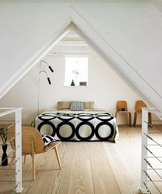 an attic bedroom with white walls and wood flooring is furnished with black and white decor