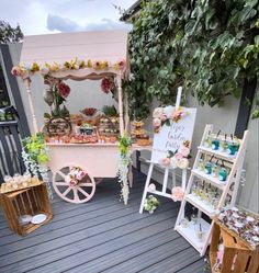 an outdoor dessert cart is set up on a deck with flowers and greenery around it