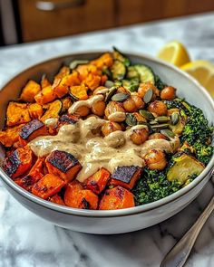 a bowl filled with vegetables and sauce on top of a marble table next to lemon wedges