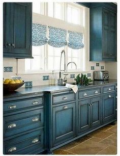 a kitchen with blue cabinets and tile flooring, along with a bowl of fruit on the counter