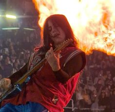 a man with long hair holding a guitar in front of a fire filled stadium full of people