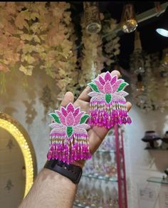 a hand holding two pink and green earrings