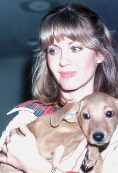 a woman holding a small brown dog in her arms and wearing a red plaid shirt