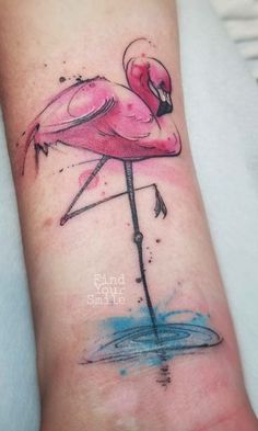 a pink flamingo tattoo on the left arm and wrist with watercolor paint splatters