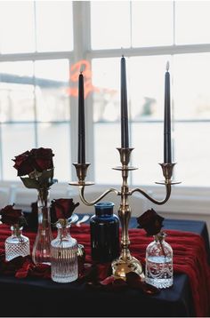 a table topped with candles and vases filled with flowers next to each other on top of a red cloth covered table