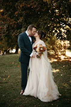 a bride and groom standing in front of a tree with their arms around each other