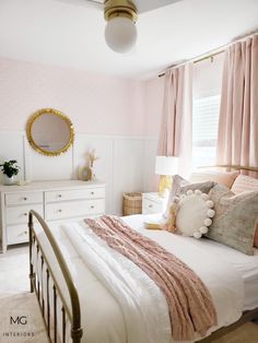 a bedroom with pink walls and white bedding, gold mirror on the wall above the bed