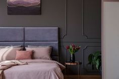 a bed with pink and grey sheets in a bedroom next to a painting on the wall