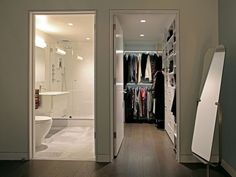 an open door leading to a walk in closet with clothes on hangers and a toilet