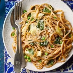 a white plate topped with pasta and veggies next to a knife and fork