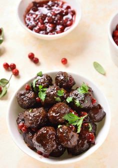 two white bowls filled with meatballs and cranberry sauce on top of a table