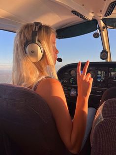 a woman sitting in the cockpit of an airplane with headphones on and pointing at something