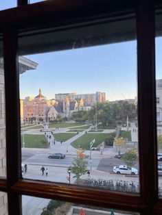 the view from inside a window looking out onto a city street and park with people walking on it