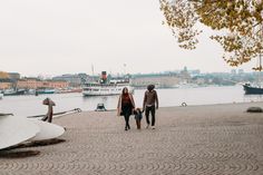 a man and woman are walking along the shore with their child near boats in the water