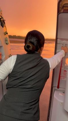 a woman opens the refrigerator door to look out at the water and sunset in the background